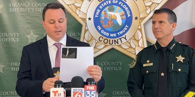 Joe Covelli, a Homicide Sergeant at the Orange County Sheriff's Office holds up a picture of the necklace during a press conference on Thursday.